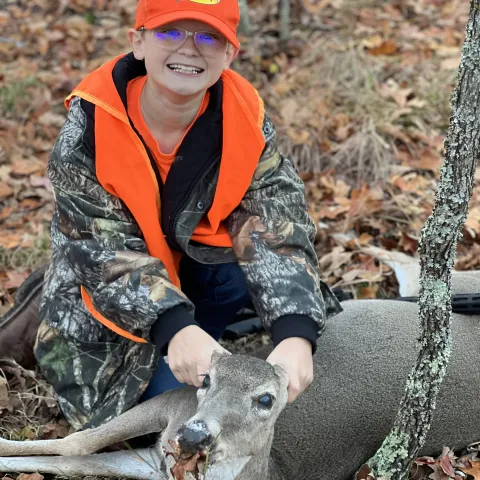 Young hunter wearing orange pictured with harvested deer.