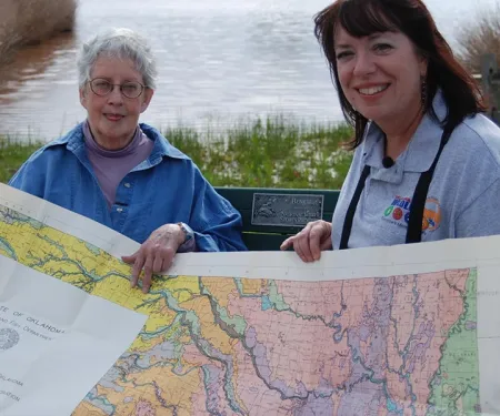 Two women looking at a ecological map of Oklahoma on a bench.