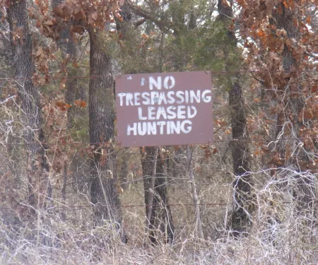 A brown sign with white lettering shows "No Trespassing Leased Hunting." 