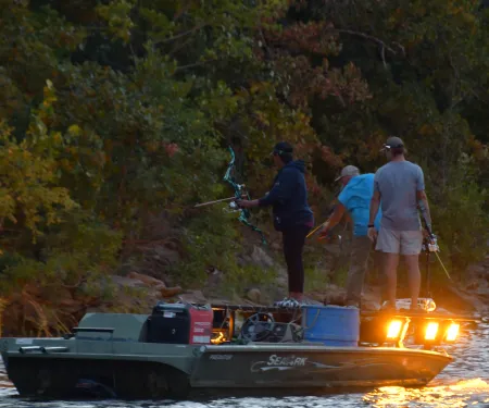 Two men and a woman stand on a boat with bows and arrows in hand. 