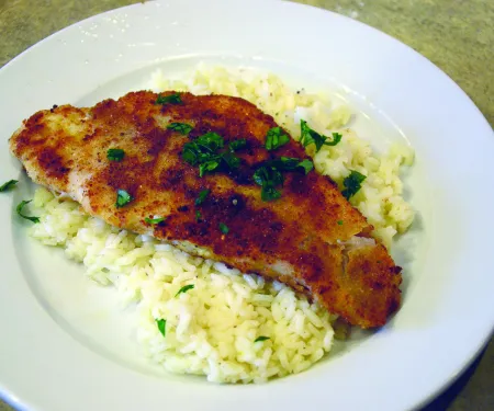 A fried fish filet on top of a plate of rice.