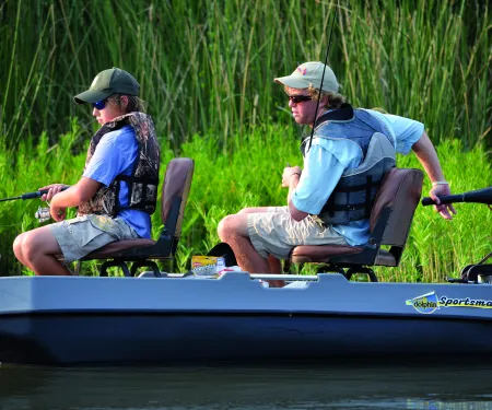 Two anglers sit in a boat with life vests on.