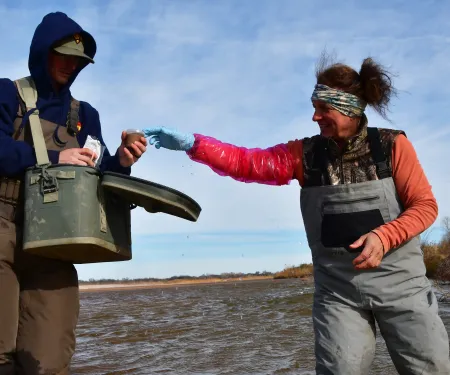 A biologist passes a soil sample to another biologist holding a small ice chest. 
