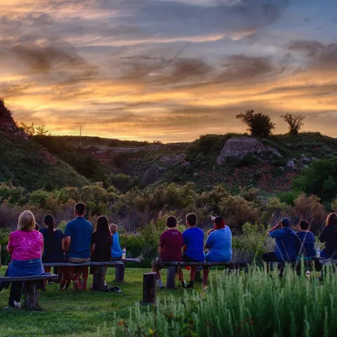 People sitting on benches looking at the horizon waiting for bats to fly over at Selman Bat Caves.