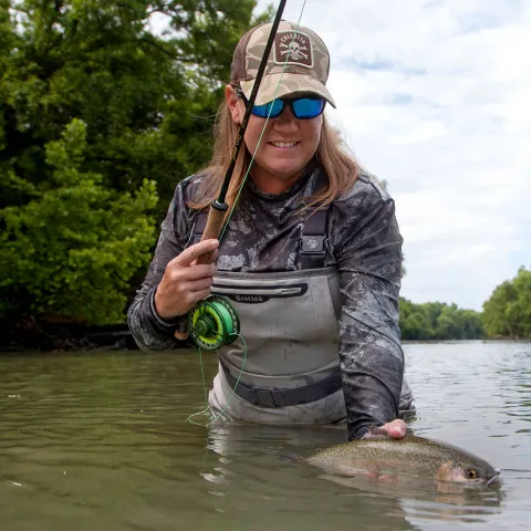 Bridget Norris Kirk fly fishing shows her trout she caught.