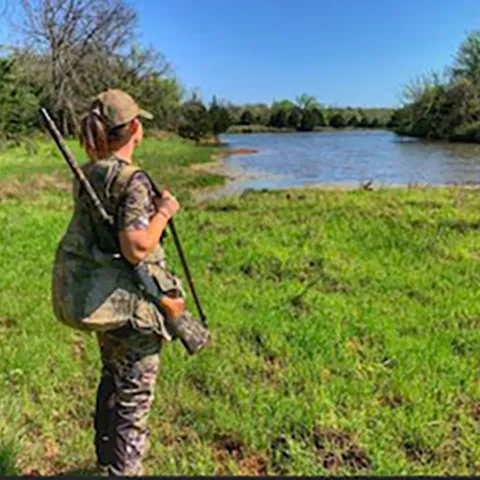 Woman in field with shotgun.