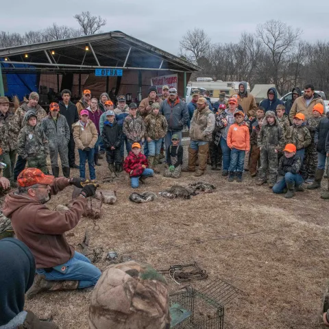 A group of people listen to a man demonstrating trapping methods. 