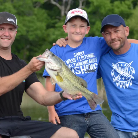 Three people in a boat with a recently caught bass