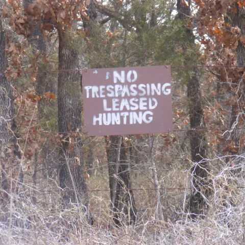 A brown sign with white lettering shows "No Trespassing Leased Hunting." 