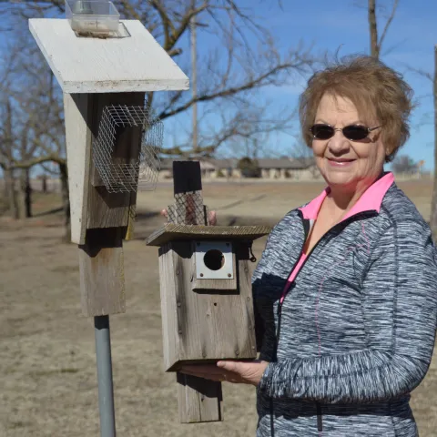 A woman stands next to a nest box while holding another nest box in her hands. 