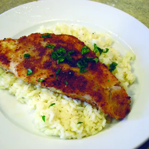 A fried fish filet on top of a plate of rice.