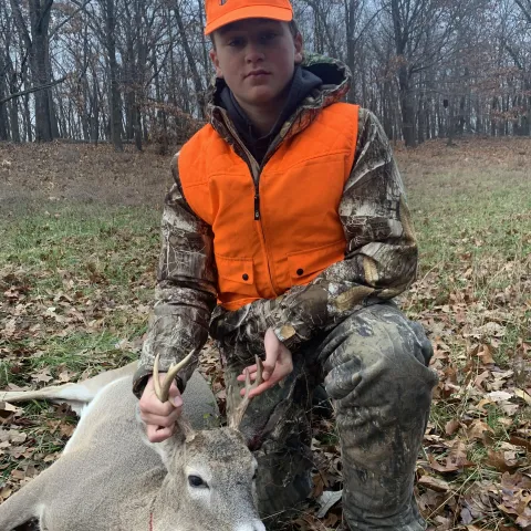 Young hunter wearing orange pictured with a harvested deer.