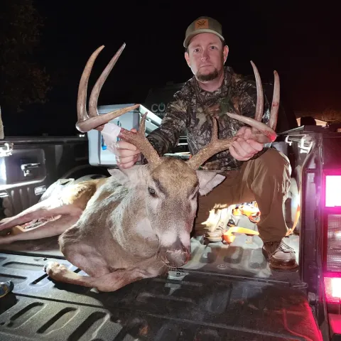 Hunter and harvested deer pictured on the bed of a pickup truck.