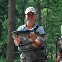 Woman holding a trout about to be stocked in stream.