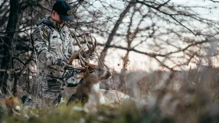 A bowhunter inspects the antlers of his harvested buck.