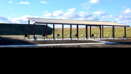 A covered pavilion at a shooting ranges with targets and a tall berm in the background.