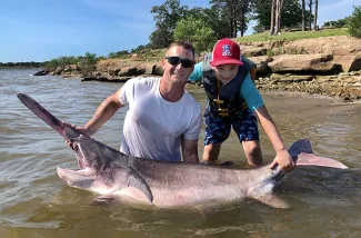 Kiefer angler Jeremiah Mefford, with help from his son, Brody, holds the state-record paddlefish he snagged at Keystone Lake on May 23, 2020. At 143 pounds, the fish busted the previous record by 10.5 pounds. (Photo by Jason Schooley/ODWC)