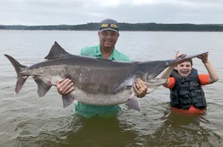 Cory James Watters of Ochelata, with help from son Stetson, 9, holds his rod-and-reel world-record paddlefish that he snagged July 23 at Keystone Lake. (Photo by Eric Brennan/ODWC)