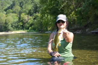 Woman holds a smallmouth bass caught in a creek.