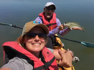 Two women fishing from a kayak with a bass.