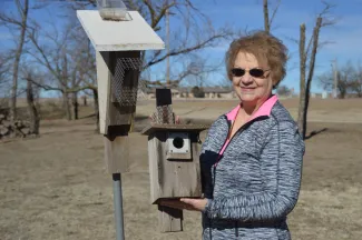 A woman stands next to a nest box while holding another nest box in her hands. 