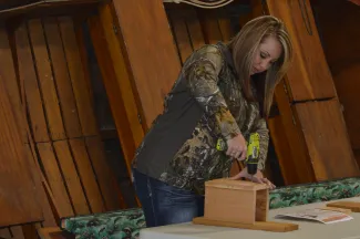 A woman attaches the front of a wooden nest box. 