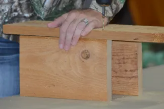 A woman attaches the back and side pieces of a wooden nest box. 