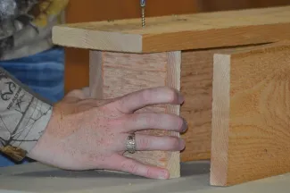 A woman attaches the floor to the back of a wooden nest box. 