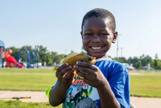 A smiling boy holds a sunfish. 