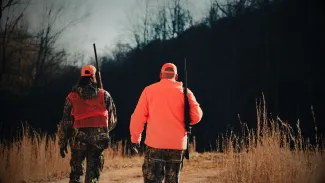 A man and woman dressed in hunter orange are walking during a hunt.