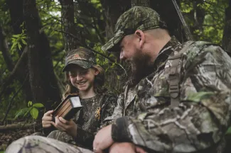 A man and girl are practicing turkey calling during a turkey hunt.