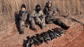 Two youth hunters and their guide are sitting behind a row of harvested ducks.
