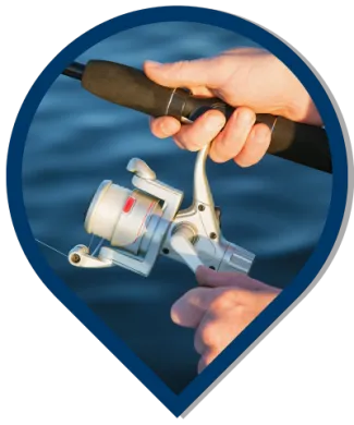 A close-up of hands holding a fishing reel over water, cropped in the shape of a map icon.