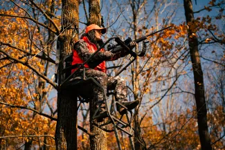 A female hunter is sitting in a tree stand.