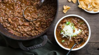 A pot of chili next to a bowl of chili.