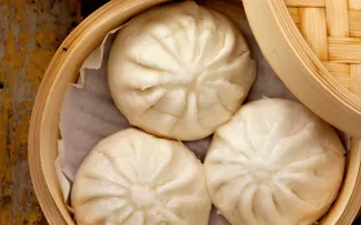 Three steamed buns in a bamboo container.