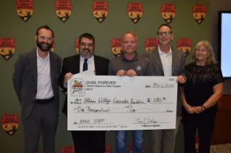 A group of people are holding a large $1,000 check donated by the Oklahoma Chapter of Quail Forever to support the Oklahoma Scholastic Shooting Sports Program.