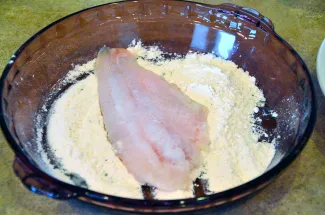 A fish filet is resting on a pan of flour.