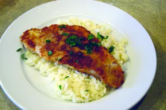 A fried fish filet on top of a plate of rice.