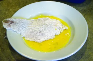A floured fish fillet is sitting in a bowl of beaten eggs.