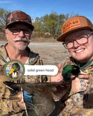 Two men hold a brown duck with a green head. 