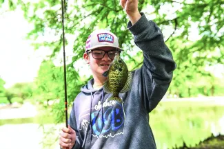 An Oklahoma student shows off his catch, holding the fish on the line in front of him.