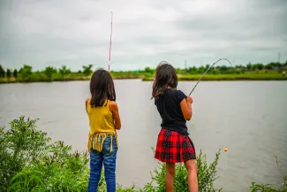 Two girls are standing on the shore of a lake and fishing.