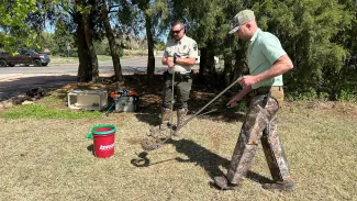An Oklahoma Game Warden Academy student is learning how to handle venomous snakes as he gently uses a grabber to lift the snake into a bucket. 
