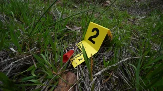 A photograph of poaching evidence. A yellow evidence marker with the number two on it is next to an empty shotgun shell on grass.