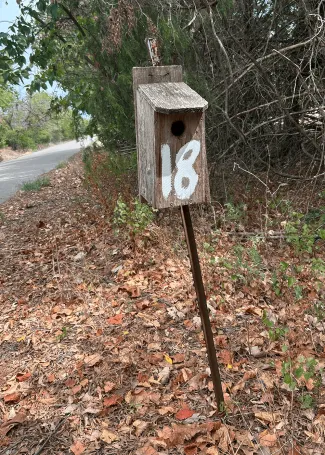 A simple wood box birdhouse with the number 18 spray painted on it.